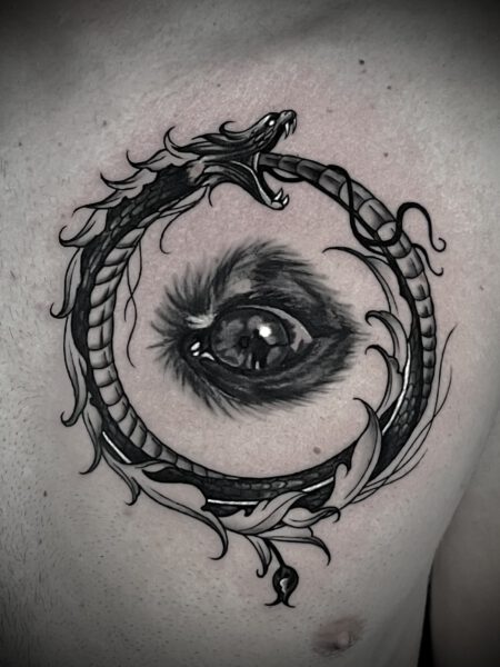 Tattoo eines geschlossenen Kreises, der von einem Drachen umschlungen wird, mit einem detaillierten, realistischen Auge in der Mitte. Der Drache hat eine dynamische Pose und zeigt seine Zähne, während der Hintergrund leicht rosa schattiert ist.