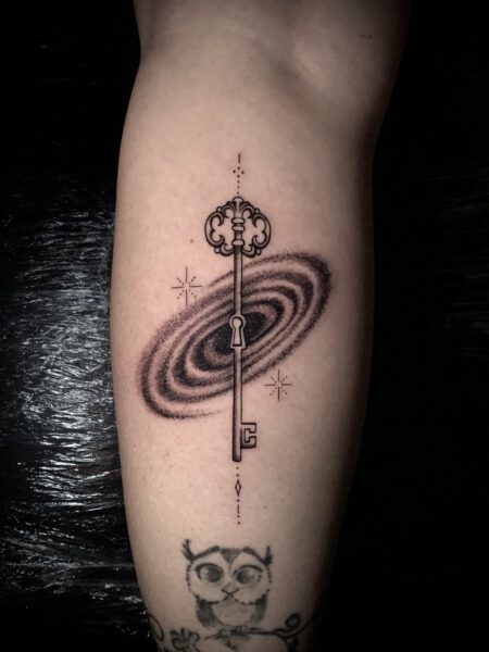 Tattoo Stil Fineline - Schlüssel mit einer Galaxie, die mit Sternen verziert ist.